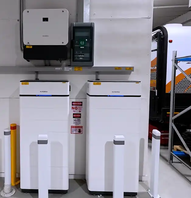 Sungrow inverter and two stacked battery units installed on a wall with protective bollards