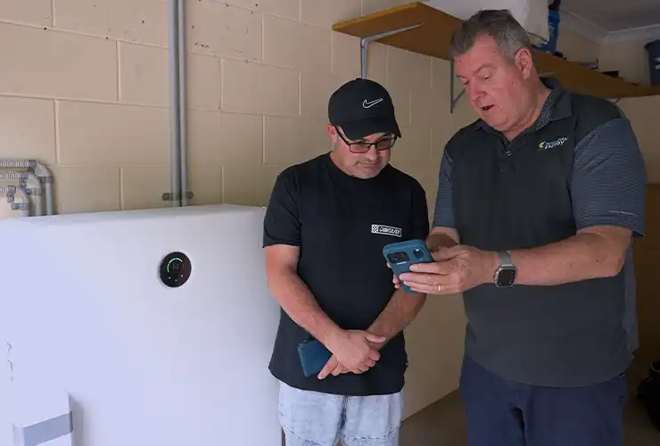 Replenishable Energy team member showing a customer a home battery's app on a phone in a garage