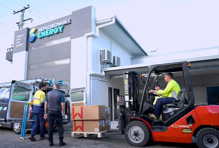 Replenishable Energy team loading boxed solar equipment from a forklift into a branded van outside the company building