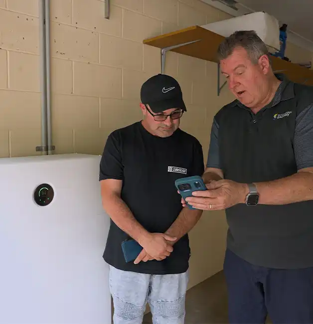 Replenishable Energy team member showing a customer the battery monitoring app on a phone beside a home battery