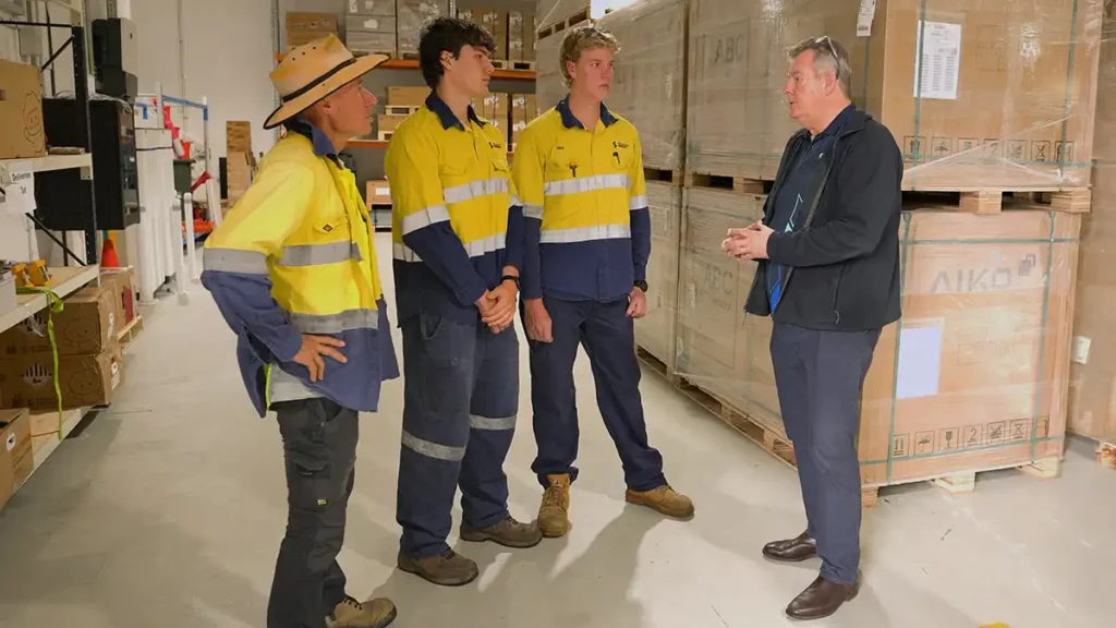 Replenishable Energy installers talking with a team member in the warehouse beside pallets of AIKO solar panels