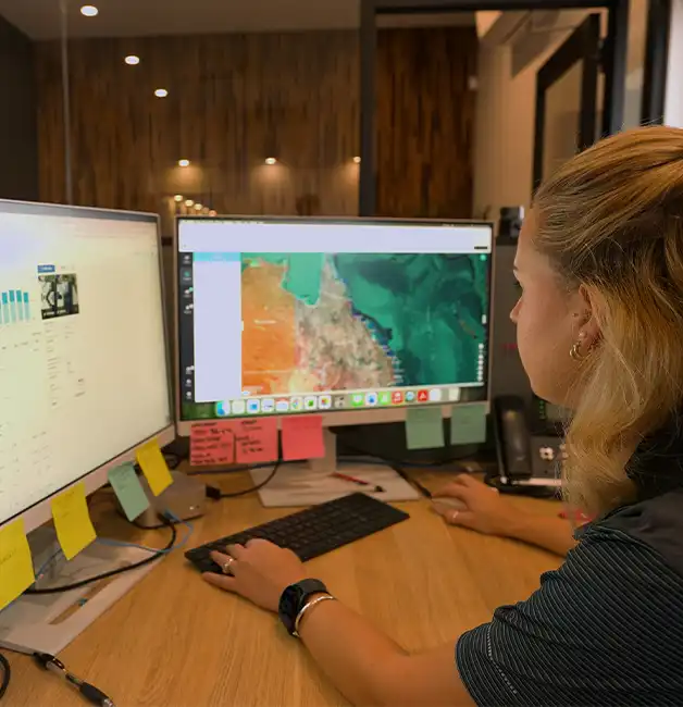Replenishable Energy team member at her desk reviewing solar system data and a regional map on dual monitors