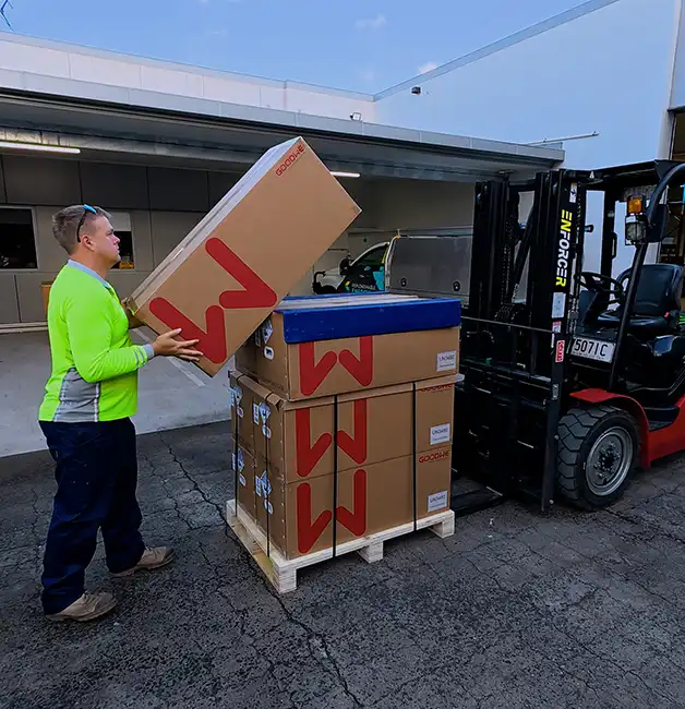 Replenishable Energy team member loading boxed solar equipment onto a pallet beside a forklift at the warehouse